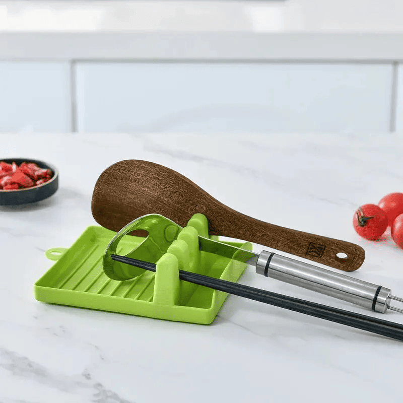 suporte e descanso para tampas e espátulas verde com colher de madeira, colher de metal, 2 hashis pretos e mini tomates ao lado