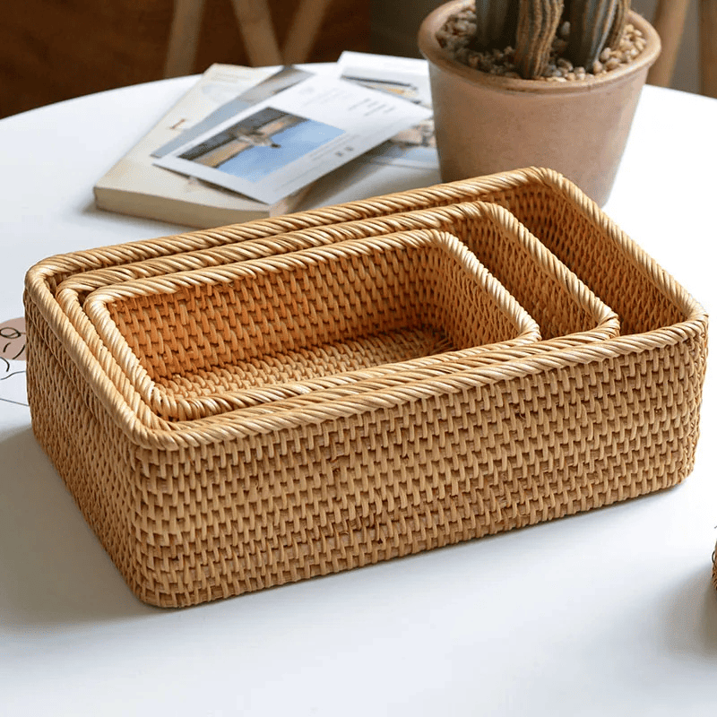 3 cestos de palha rattan de tamanhos diferentes empilhados sobre mesa branca, com vaso de planta e livro atrás