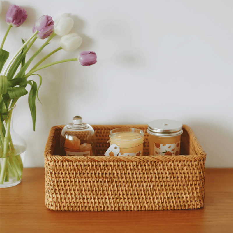 Cesto de palha rattan com produtos dentro sobre mesa, acompanhado por vaso de plantas ao lado